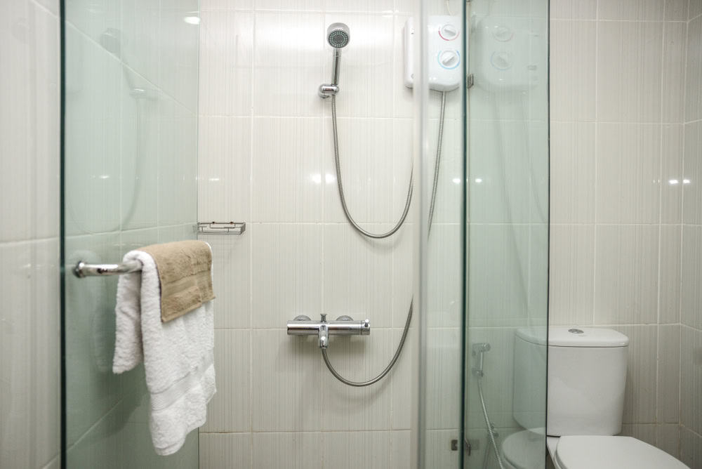 A clean bathroom designed by a renowned glass contractor in Union County, NJ, features a sleek glass-enclosed shower area with a mounted showerhead and control panel. A white toilet sits beside the shower, while a towel hangs neatly on a rail against the tiled walls.